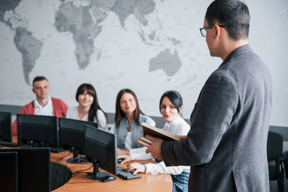 Instructor leading a team meeting in an office with computers, explaining strategies related to the Growth Navigate Funding Program.