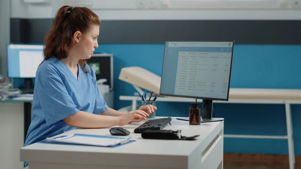Aspiring medical billing and coding professional working at a desk with coding manuals and computer software with support from grants for medical billing and coding.